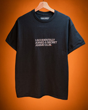 Black t-shirt with text saying I accidentally joined a secret anime club on a hanger against an orange background